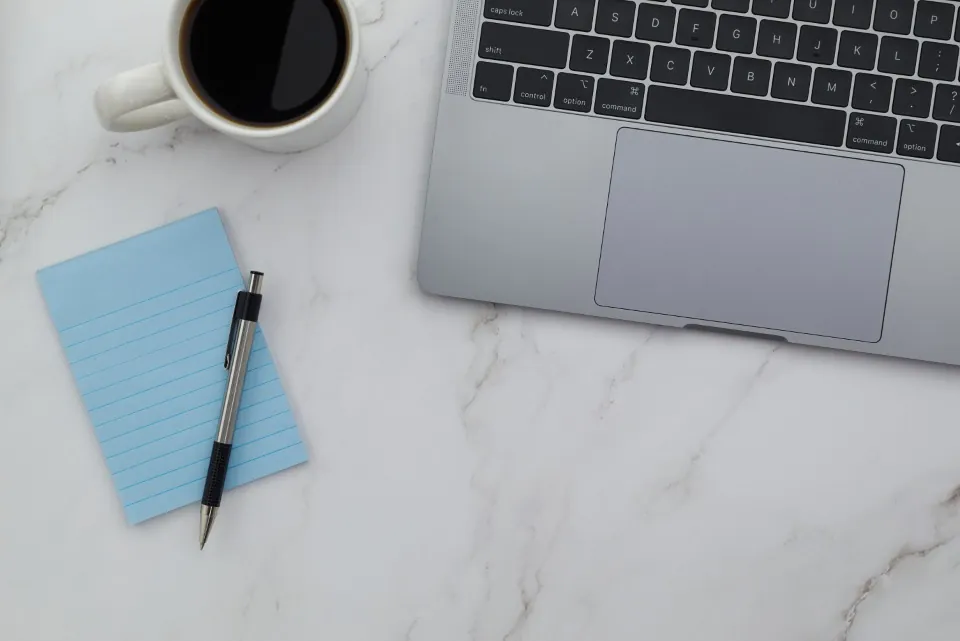 Portátil, cuaderno y café sobre una mesa de mármol
